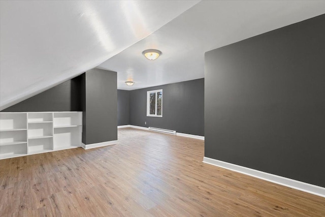 additional living space featuring light wood-type flooring, vaulted ceiling, and baseboard heating