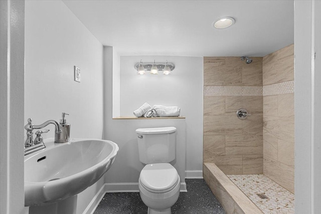 bathroom with a tile shower, sink, and toilet