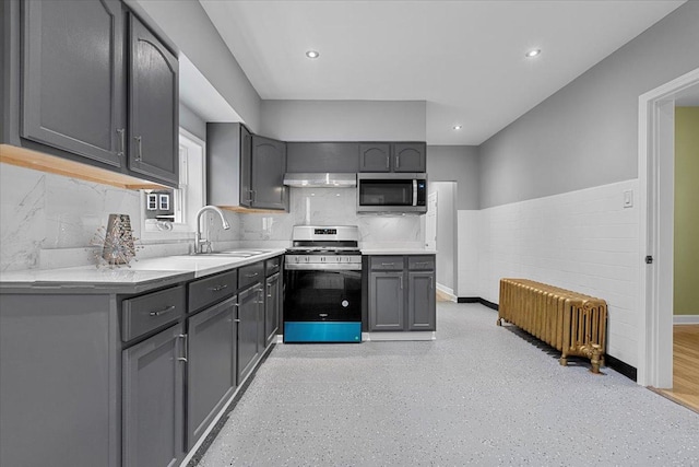 kitchen with gray cabinetry, sink, radiator heating unit, range hood, and appliances with stainless steel finishes