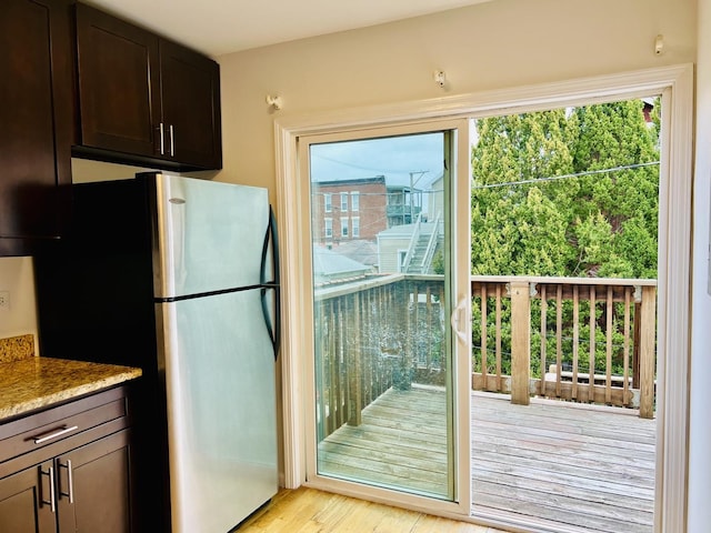 kitchen featuring stainless steel fridge, dark brown cabinets, light hardwood / wood-style floors, and light stone counters