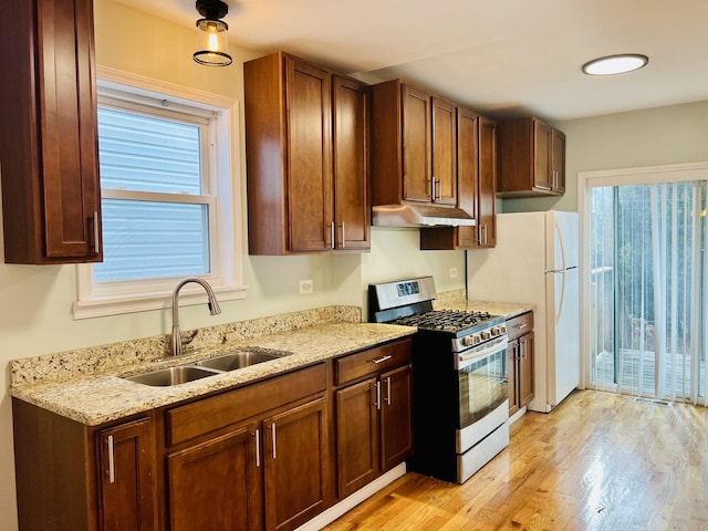 kitchen with light stone counters, gas range, sink, light hardwood / wood-style flooring, and white fridge