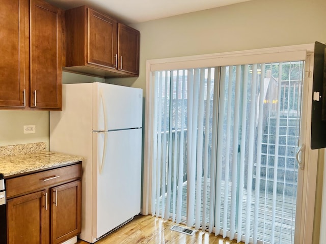 kitchen featuring white fridge, light stone counters, light wood-type flooring, and a wealth of natural light