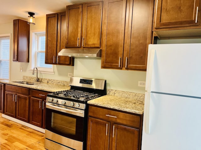 kitchen with sink, stainless steel gas range, light stone counters, white fridge, and light hardwood / wood-style floors