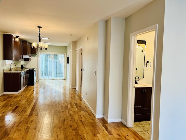 hallway featuring light wood-type flooring, an inviting chandelier, and sink