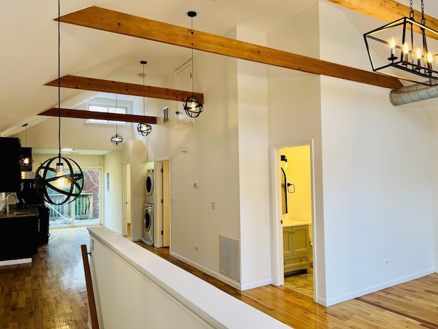 corridor featuring beamed ceiling, light hardwood / wood-style floors, stacked washing maching and dryer, and high vaulted ceiling