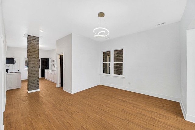 unfurnished room featuring sink, light hardwood / wood-style flooring, and decorative columns