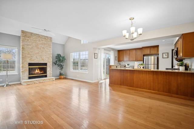 kitchen featuring lofted ceiling, a stone fireplace, stainless steel appliances, decorative light fixtures, and light wood-type flooring