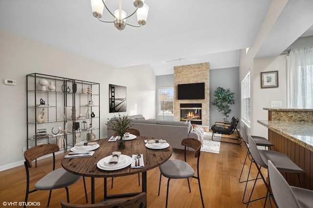 dining area featuring lofted ceiling, a notable chandelier, a stone fireplace, and wood-type flooring