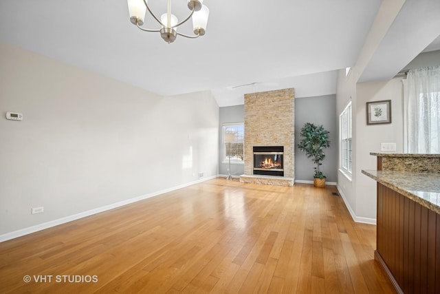 unfurnished living room featuring a fireplace, light hardwood / wood-style floors, a chandelier, and vaulted ceiling