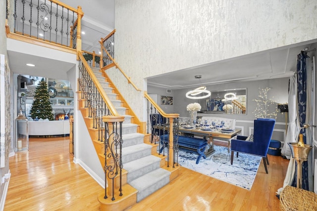 stairway featuring wood-type flooring, a towering ceiling, and a notable chandelier