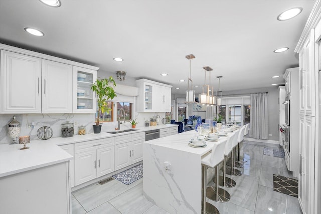 kitchen featuring a wealth of natural light, sink, a kitchen island, decorative light fixtures, and white cabinets