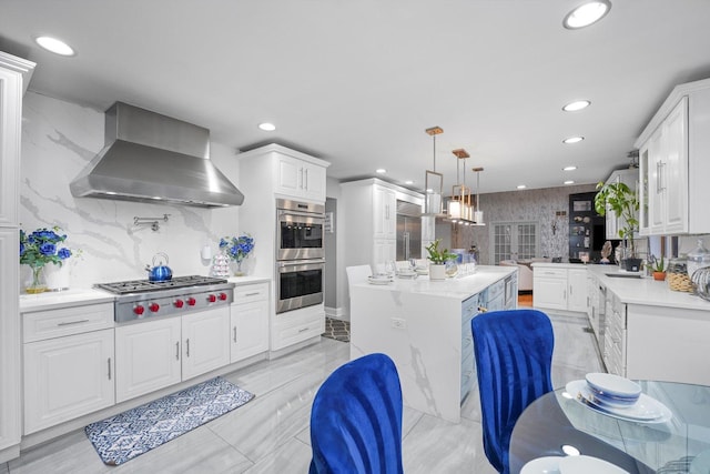 kitchen featuring white cabinets, wall chimney exhaust hood, decorative light fixtures, and appliances with stainless steel finishes