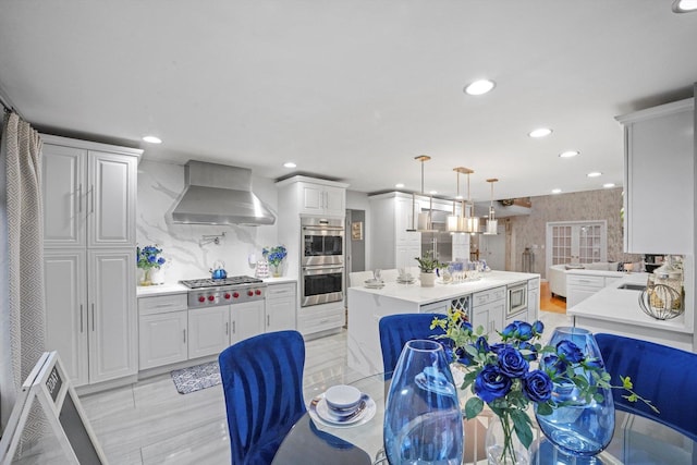 kitchen featuring tasteful backsplash, stainless steel appliances, hanging light fixtures, and wall chimney exhaust hood