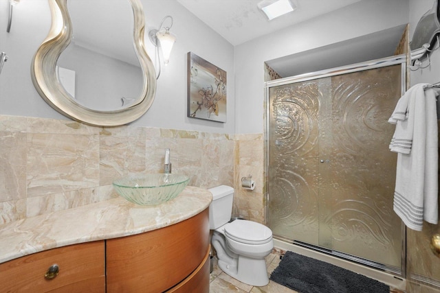 bathroom with vanity, a shower with door, toilet, and tile walls