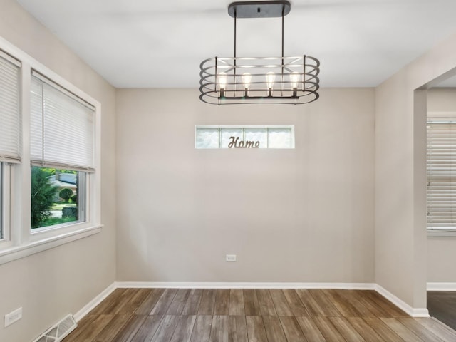 unfurnished dining area featuring a chandelier, plenty of natural light, and wood-type flooring