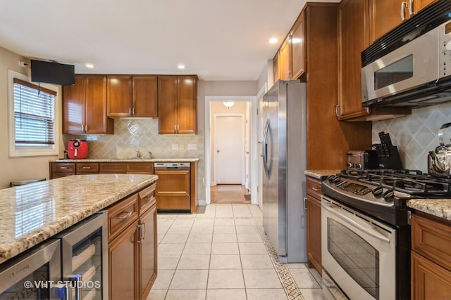 kitchen featuring appliances with stainless steel finishes, brown cabinetry, light tile patterned flooring, and light stone counters