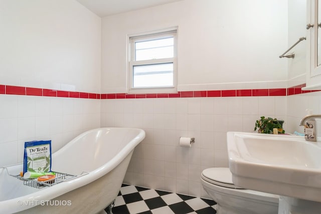 full bathroom featuring tile walls, toilet, a sink, a freestanding tub, and tile patterned floors