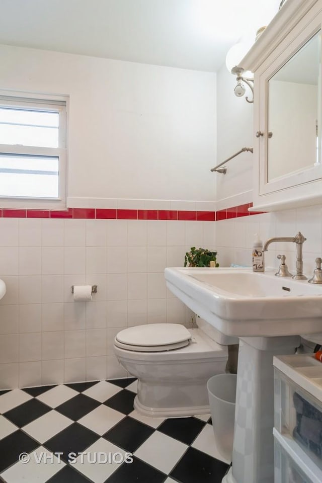 half bath featuring toilet, a wainscoted wall, tile walls, and tile patterned floors