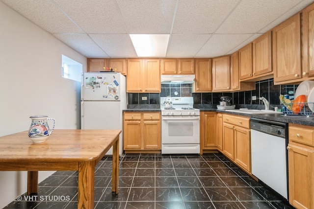 kitchen with white appliances, dark countertops, a sink, under cabinet range hood, and backsplash