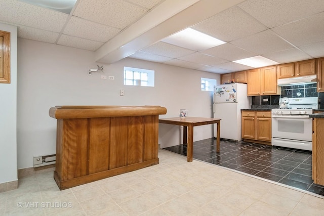 kitchen with dark countertops, white appliances, a drop ceiling, under cabinet range hood, and tile patterned floors