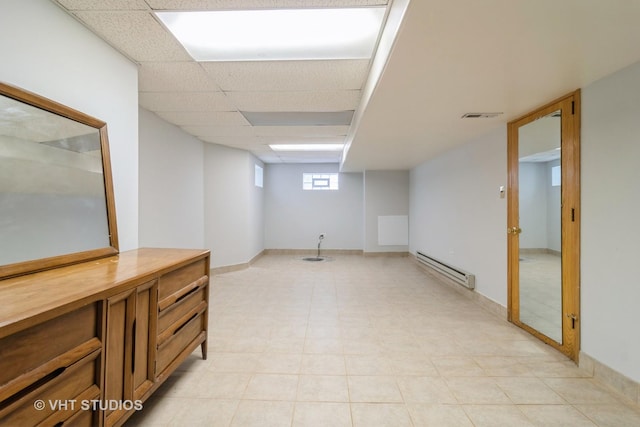 basement with a drop ceiling, a baseboard radiator, visible vents, and baseboards