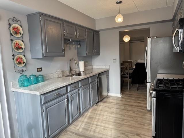 kitchen with gray cabinetry, pendant lighting, sink, light hardwood / wood-style flooring, and appliances with stainless steel finishes