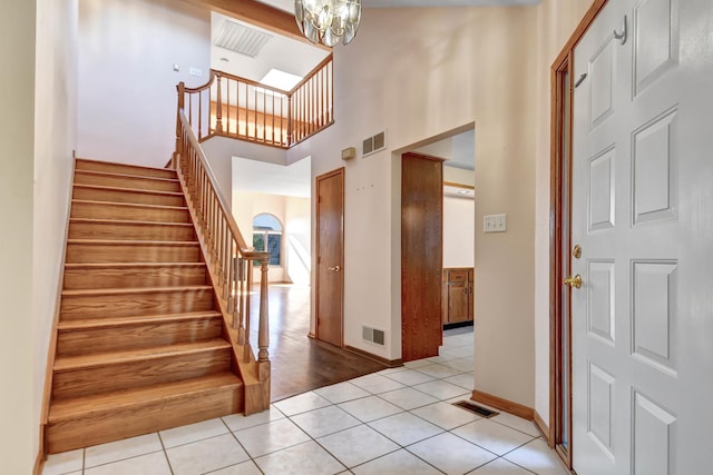 stairway with tile patterned flooring, a notable chandelier, and a towering ceiling