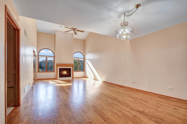 unfurnished living room with vaulted ceiling, ceiling fan with notable chandelier, and light wood-type flooring