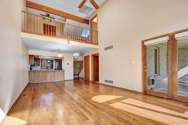 unfurnished living room featuring a towering ceiling, heating unit, light hardwood / wood-style flooring, and ceiling fan