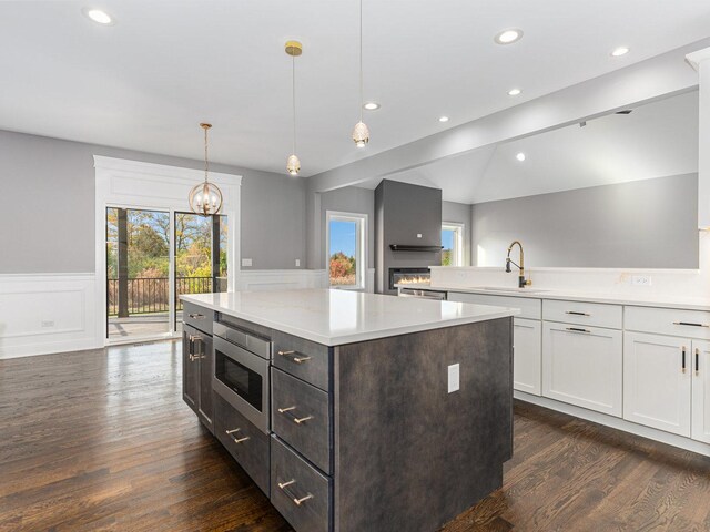 kitchen featuring a wealth of natural light, built in microwave, sink, decorative light fixtures, and white cabinets