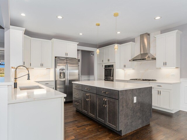 kitchen featuring sink, wall chimney exhaust hood, decorative light fixtures, a kitchen island, and appliances with stainless steel finishes