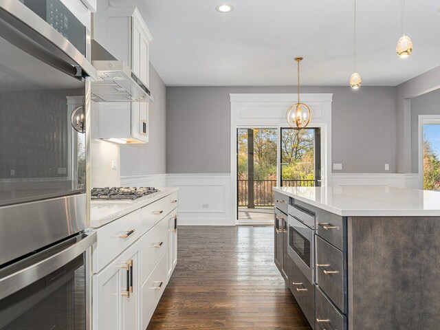 kitchen with white cabinetry, wall chimney exhaust hood, dark hardwood / wood-style floors, decorative light fixtures, and a kitchen island