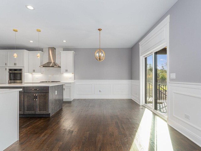 kitchen with wall chimney range hood, cooktop, oven, decorative light fixtures, and white cabinets