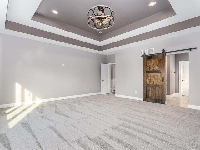 spare room with a tray ceiling, a barn door, and light carpet