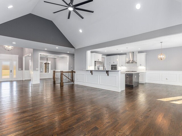 unfurnished living room with ceiling fan with notable chandelier, dark hardwood / wood-style floors, and high vaulted ceiling