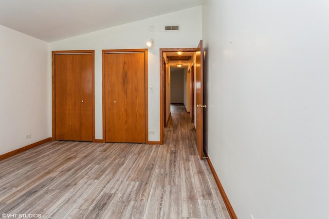 unfurnished bedroom with light wood-type flooring, lofted ceiling, and two closets