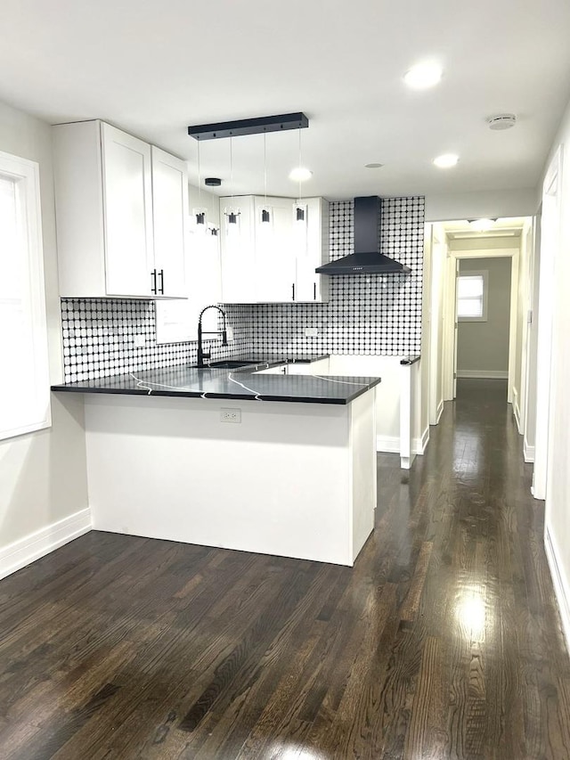 kitchen with white cabinetry, hanging light fixtures, wall chimney range hood, and a peninsula