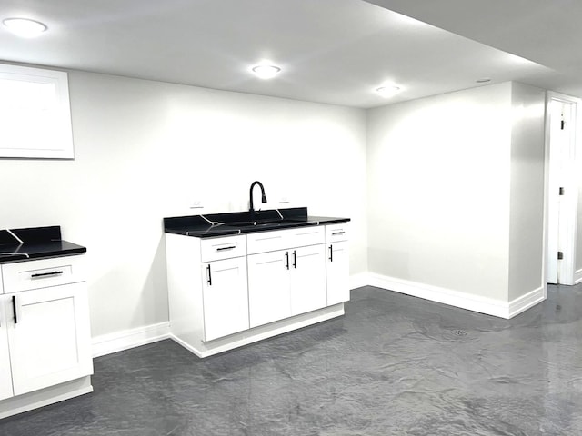 kitchen with finished concrete flooring, baseboards, white cabinets, dark countertops, and a sink