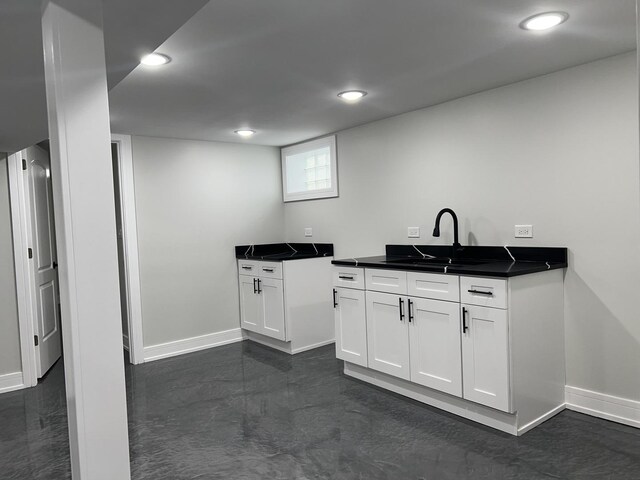 kitchen with dark countertops, white cabinets, a sink, and baseboards