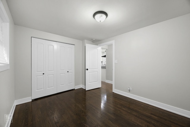 unfurnished bedroom with dark wood-style flooring, a closet, and baseboards