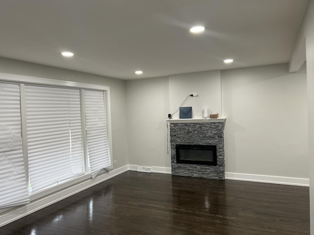 unfurnished living room featuring a stone fireplace and dark wood-type flooring