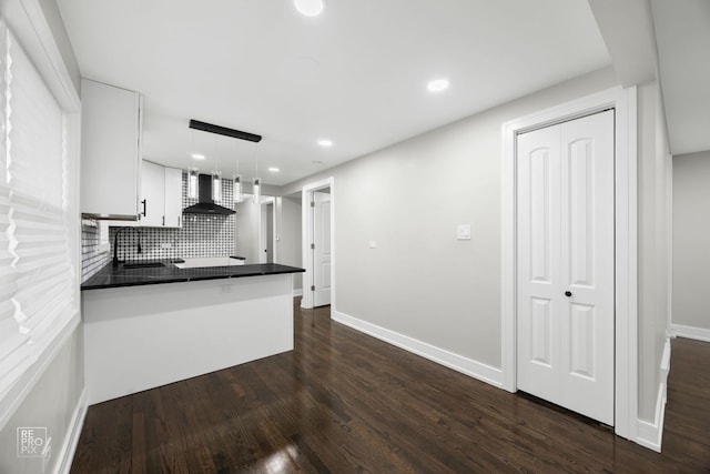 kitchen featuring dark countertops, wall chimney exhaust hood, dark wood-style flooring, white cabinetry, and pendant lighting