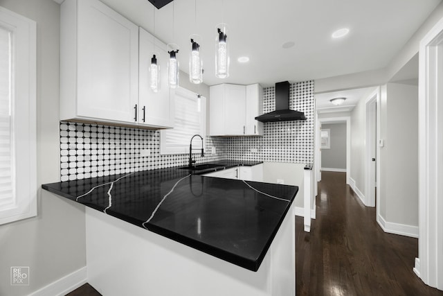 kitchen featuring white cabinets, dark countertops, wall chimney exhaust hood, hanging light fixtures, and a sink