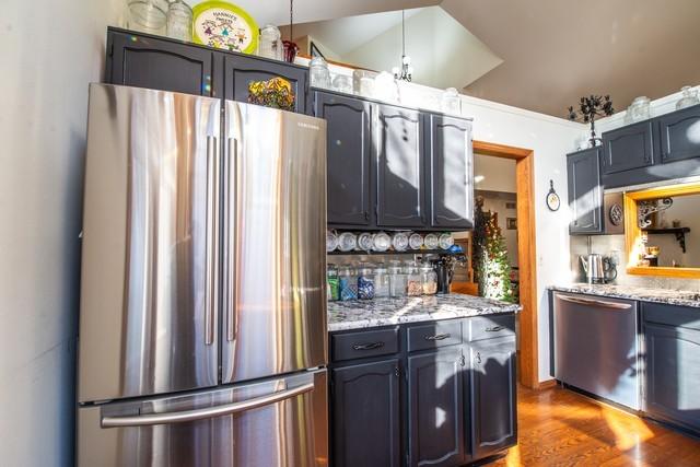 kitchen featuring hardwood / wood-style flooring, light stone countertops, lofted ceiling, and appliances with stainless steel finishes