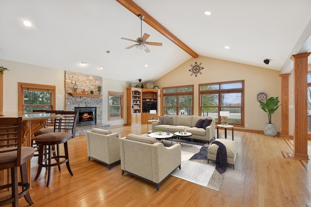 living room featuring a stone fireplace, ceiling fan, light wood-type flooring, a wealth of natural light, and beam ceiling