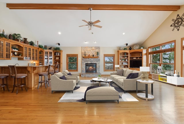 living room featuring ceiling fan, a stone fireplace, beamed ceiling, high vaulted ceiling, and light hardwood / wood-style floors