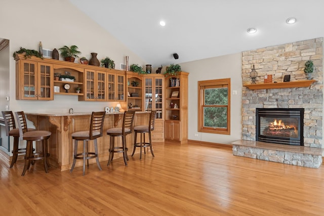 bar with lofted ceiling, a stone fireplace, and light wood-type flooring