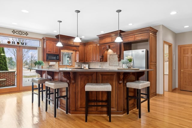 kitchen featuring decorative light fixtures, black microwave, a breakfast bar area, and light hardwood / wood-style flooring