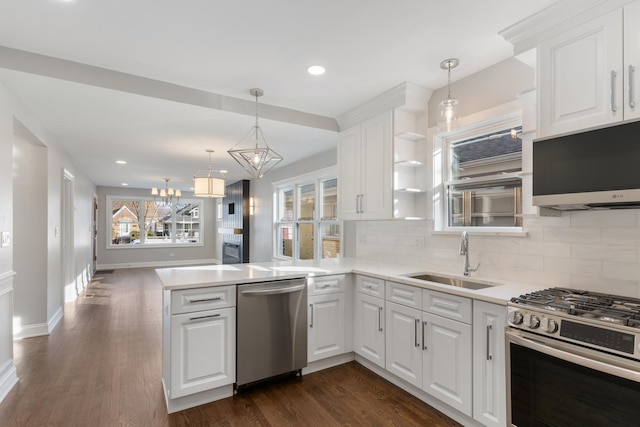 kitchen featuring decorative light fixtures, sink, white cabinets, kitchen peninsula, and stainless steel appliances