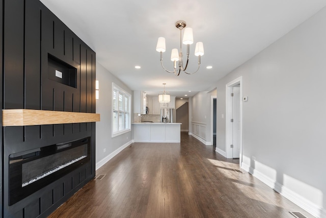 unfurnished living room featuring an inviting chandelier, a fireplace, and dark wood-type flooring